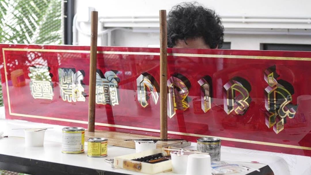 Top of man's head visible behind a sheet of glass with gilded Chinese and Thai characters set on a red background.