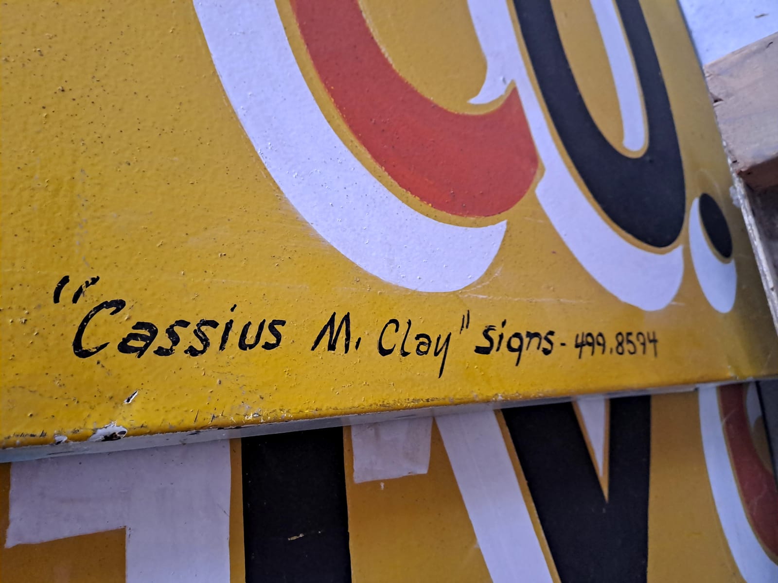 Portion of a sign painted in red, black, and white on yellow, signed "Cassius M. Clay Signs, 499.8594".