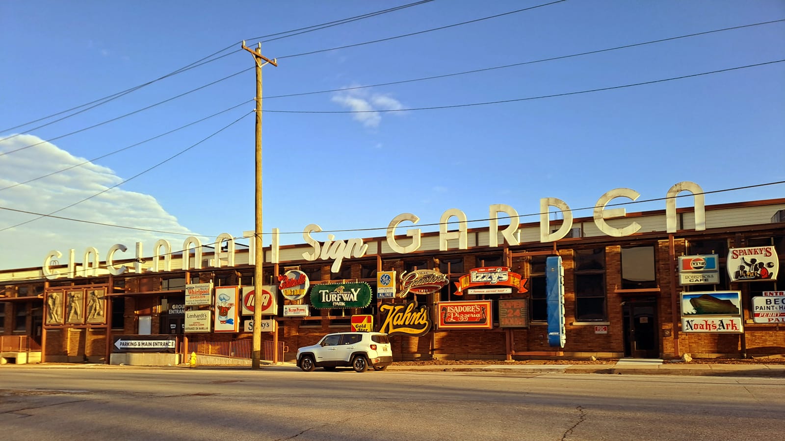 Low building with numerous signs mounted to the front, and with huge white letters protruding above the roof line that say "Cincinnati Sign Garden".