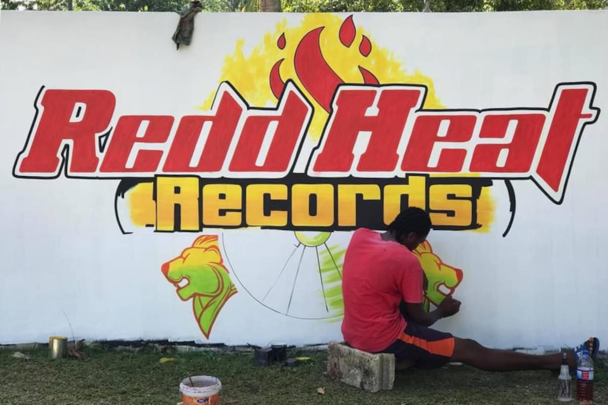 Man say on a breeze block painting a lion's head profile on a mural advertising the record label.