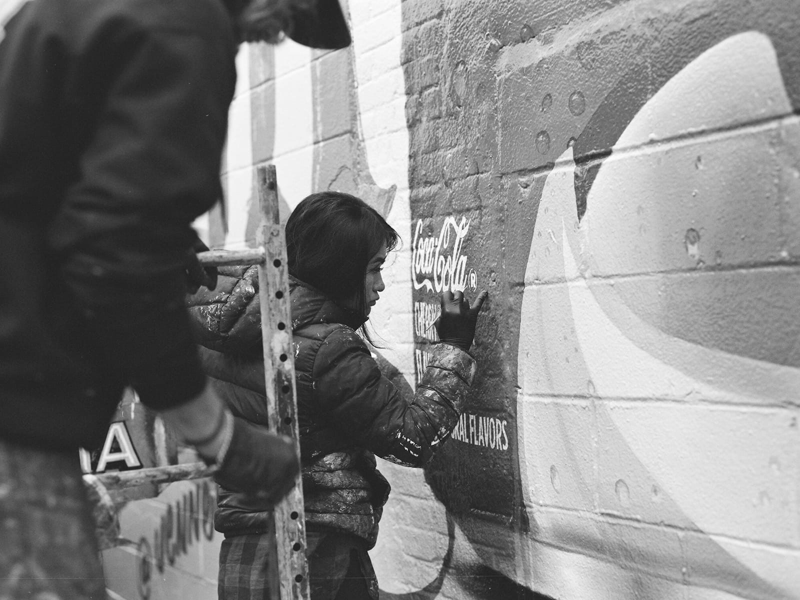 Black and white photo of a woman applying the circle to the registered trademark symbol that sits just to the right of the Coca-Cola logotype.