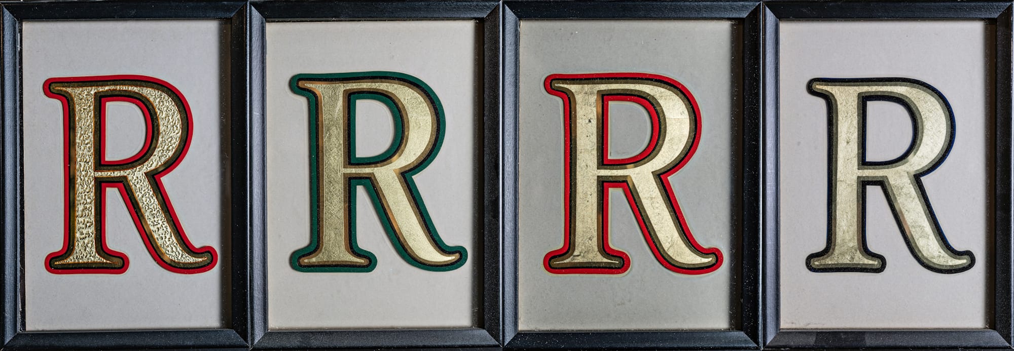 Four framed panels, each with a gilded and outlined Roman letter R inside. The outlines alternate between red and green, set outside a shiny gilded outline and the matte centred letters.