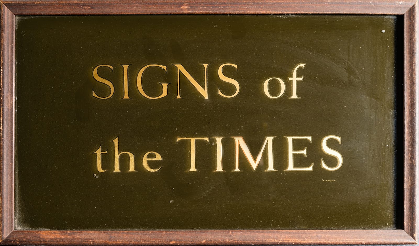 Wooden frame containing a glass panel gilded with "SIGNS of the TIMES" in Roman lettering.
