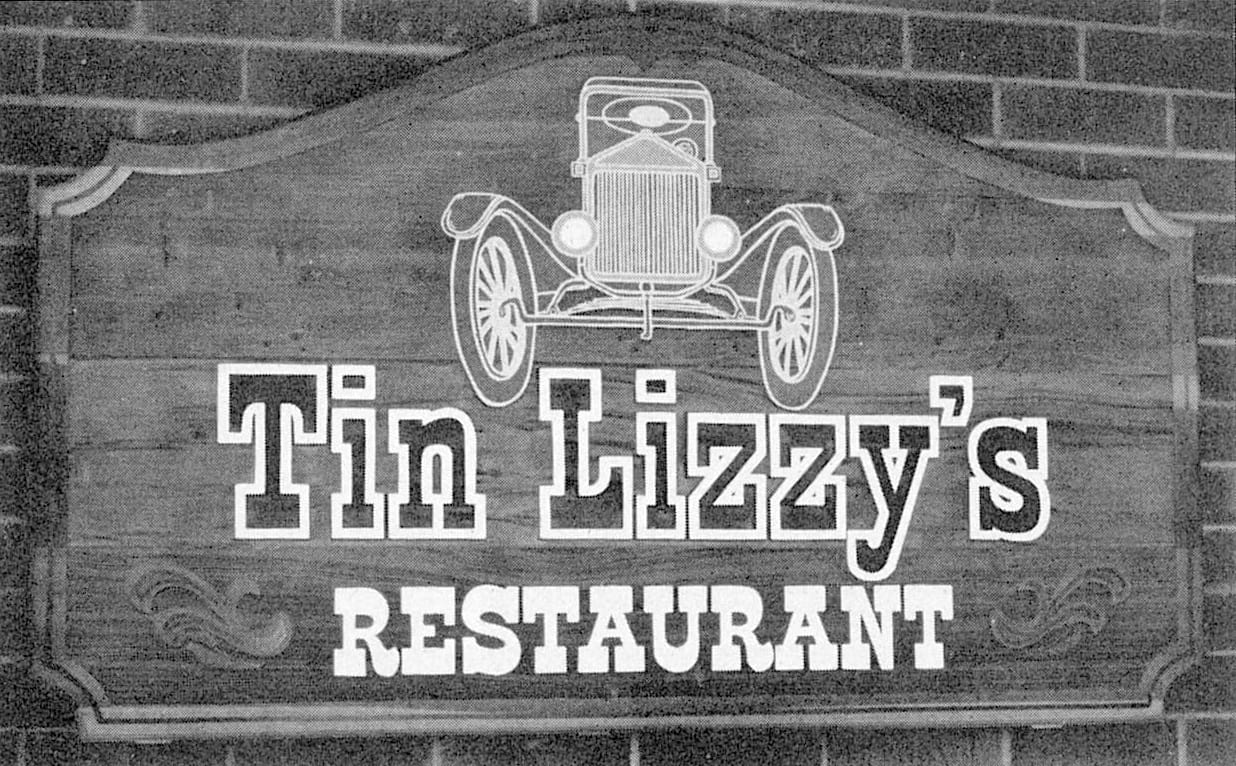 Solid wooden sign board painted with with a front-on picture of a vintage car set above lettering that reads "Tin Lizzy's Restaurant". 