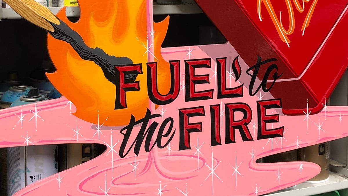 Detail of a painted panel showing a match igniting a pink liquid lettering over the top that reads "Fuel to the fire".