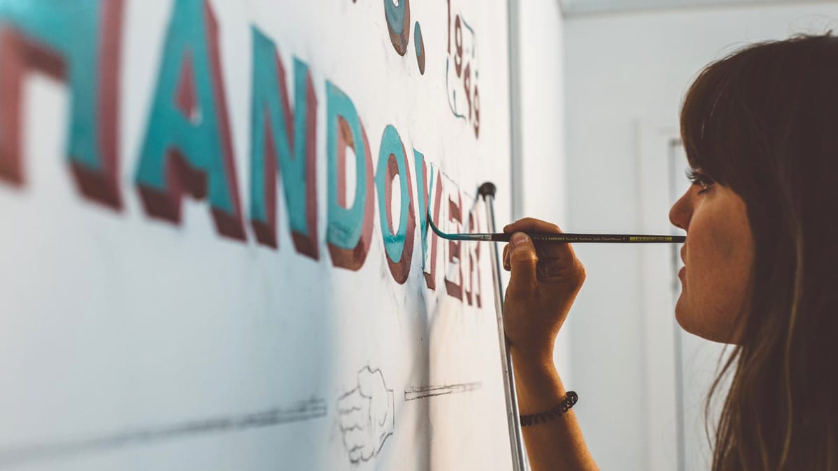 Profile view of a sign painter applying a turquoise colour to the body of letters that have been shadowed in red.