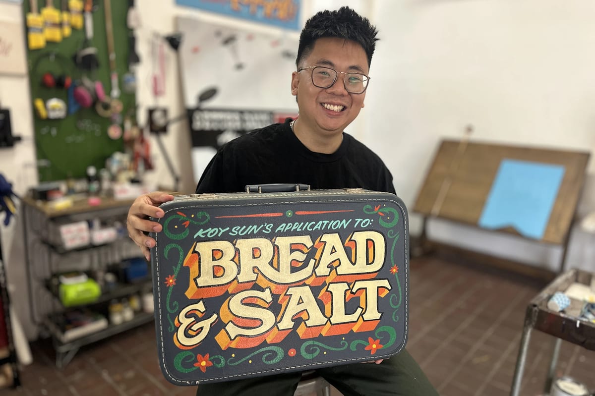 Person holding a vintage suitcase with hand-painted lettering that says "Bread & Salt".