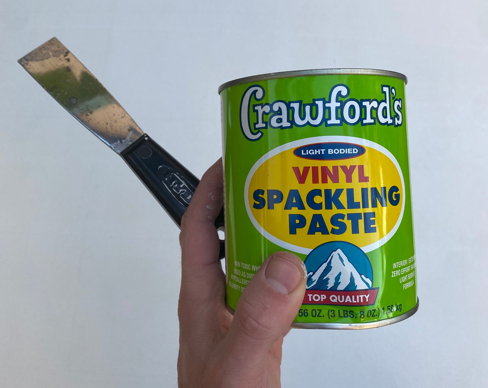 Hand holding a tin of spackling paste and spackling knife.
