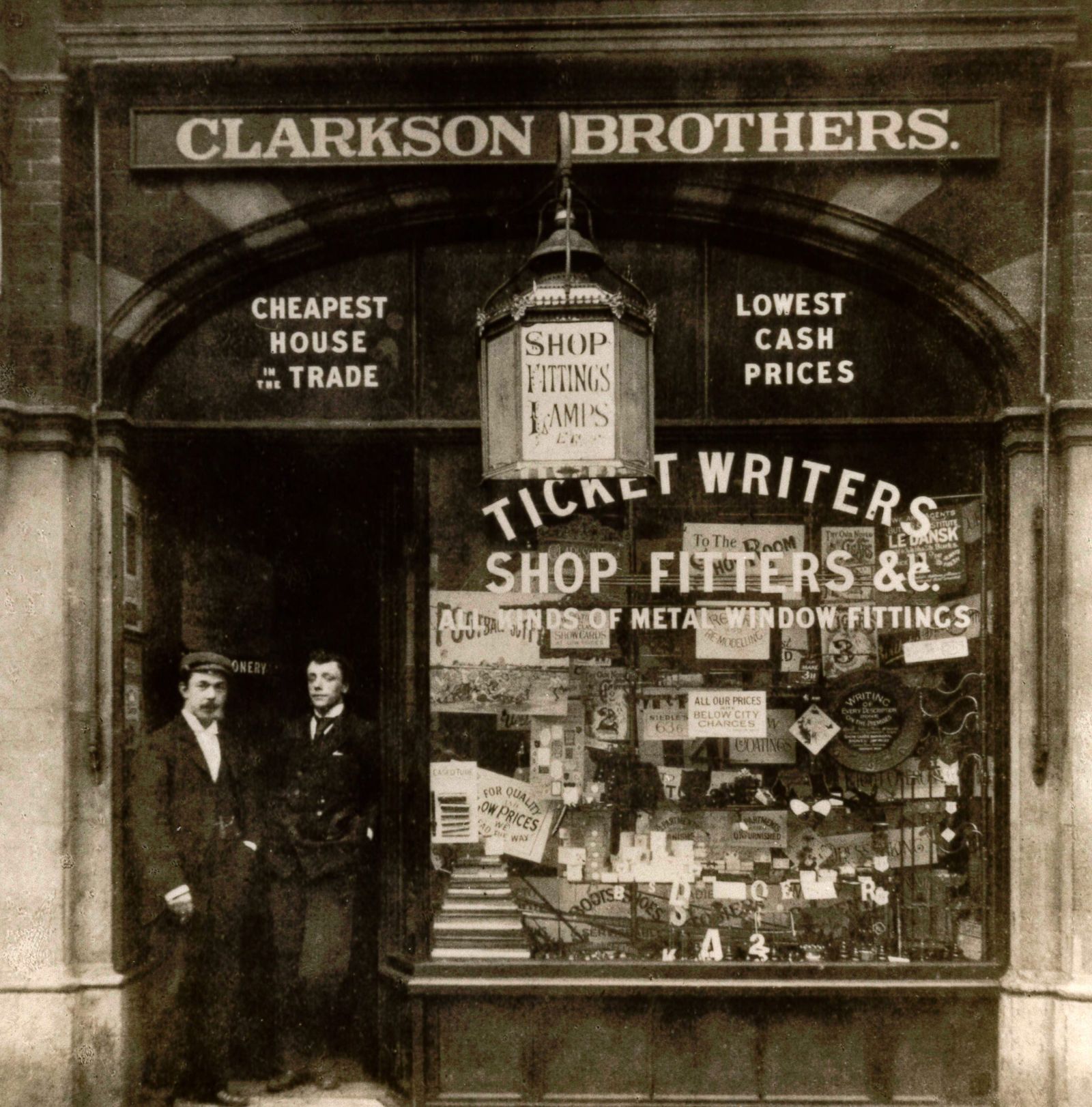 Two men standing in the doorway of a sign shop and its window displays.