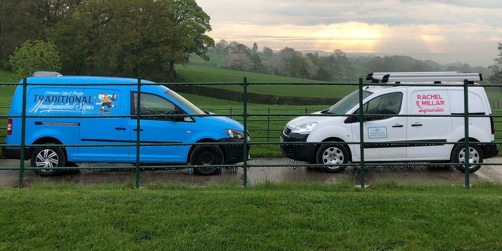 Two vans parked facing each other in a cloudy and wet countryside scene.