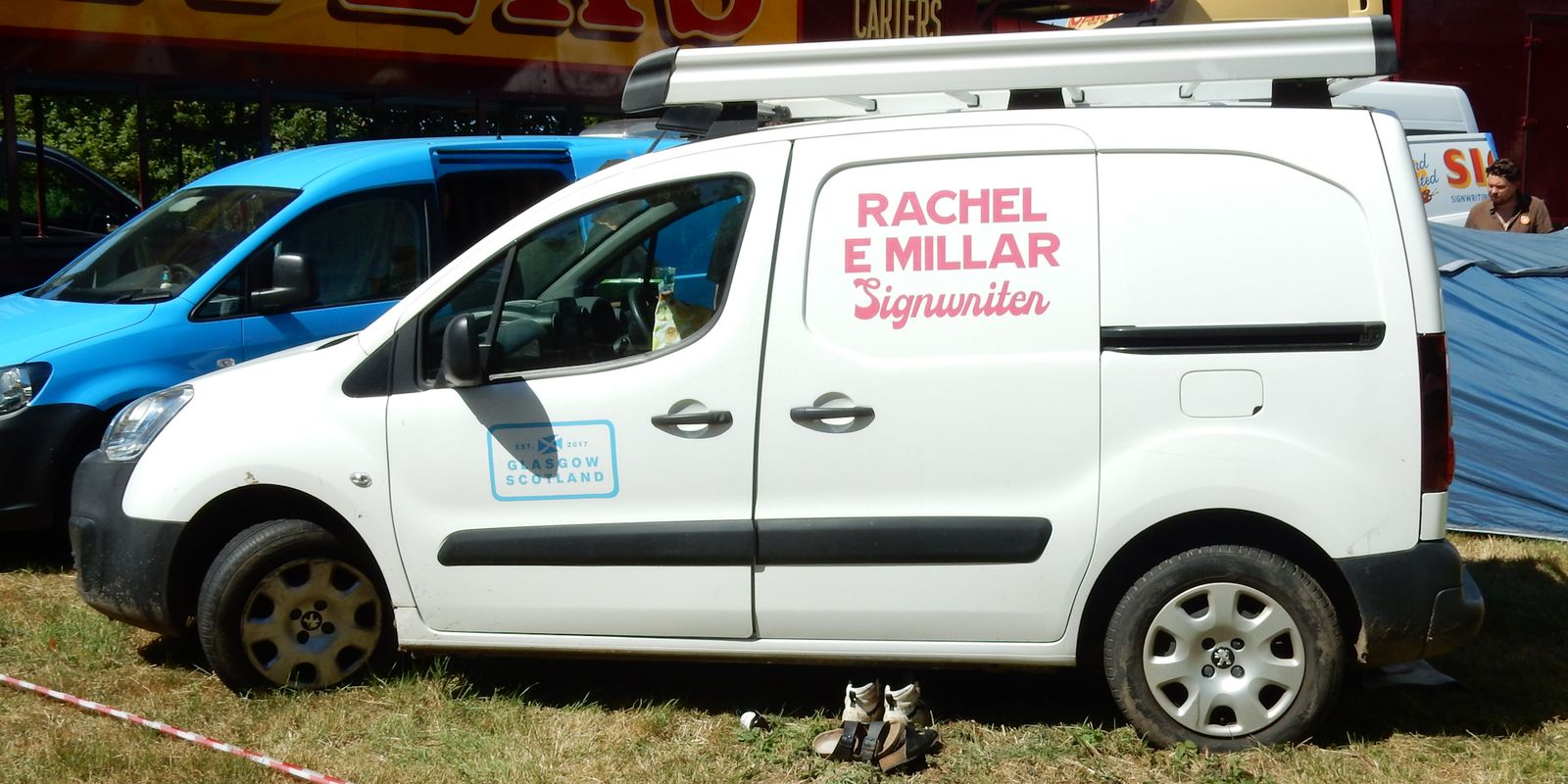 White van in bright sunshine with pink lettering painted on the side.