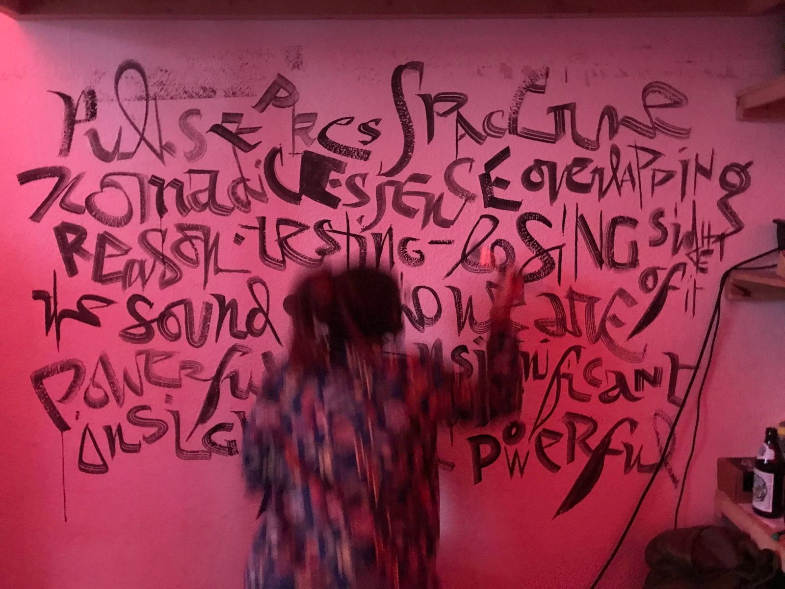 Person writing calligraphy on a wall, which is in focus while the person is blurred, suggestive of their movement.