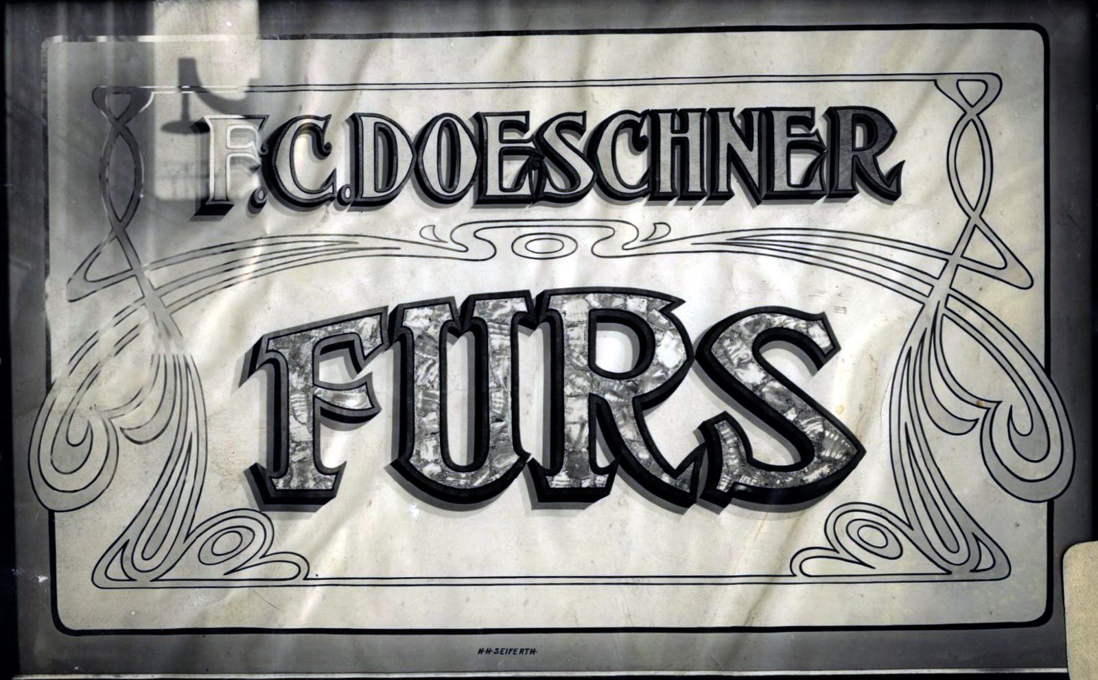 Decorated glass panel with Art Nouveau decoration surrounding lettering that reads "F.C. Doeschner Furs".