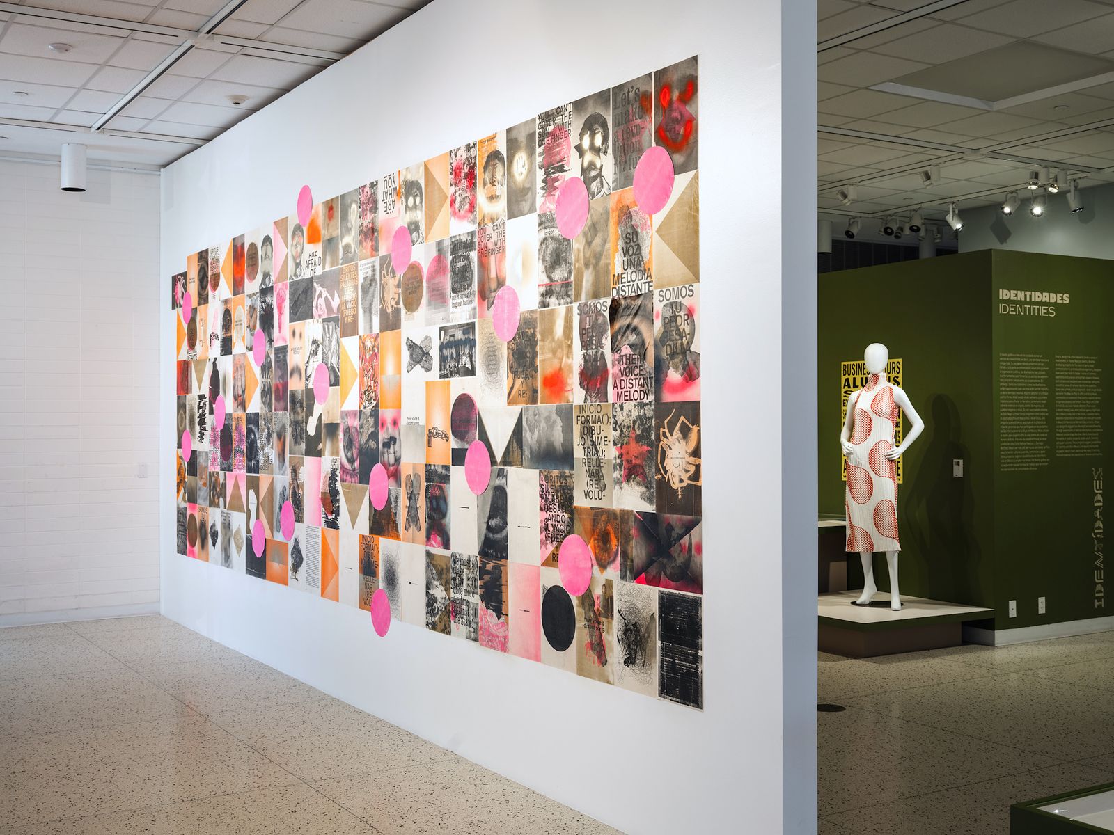 Gallery setting with a mural piece covering almost the entirety of a white wall, and a mannequin in a dress.