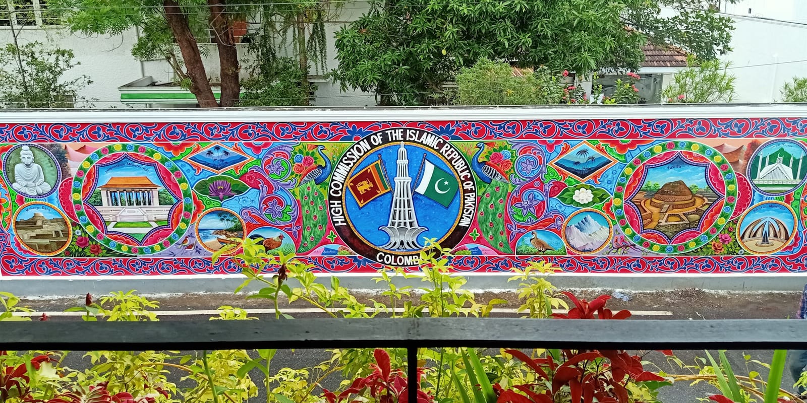 Brightly coloured decorative mural on a wall surrounding a garden, photographed from a viewing point above.