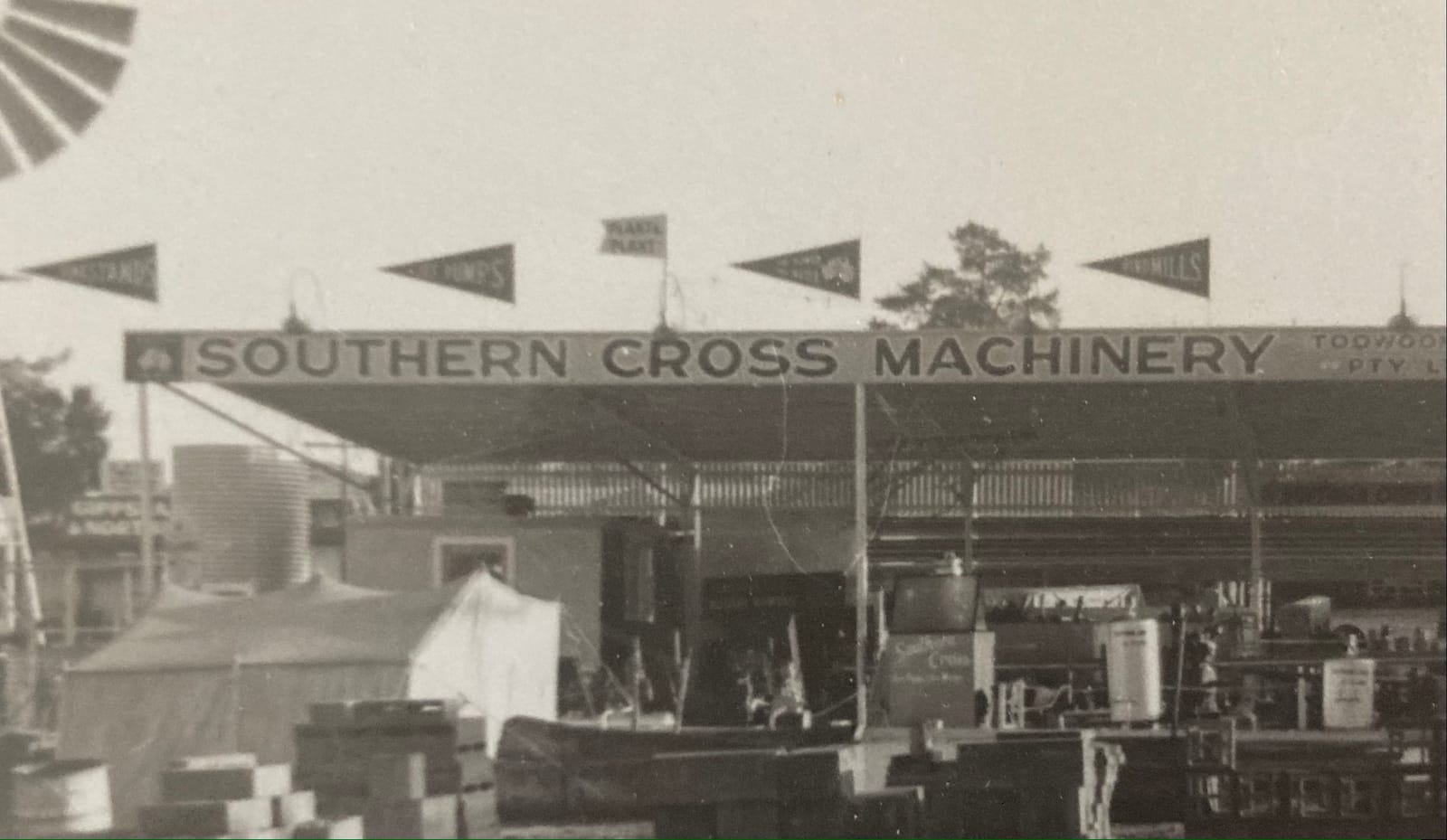 Large industrial retail space with flags flying above the flat roof which has a hand-painted awning that reads "Southern Cross Machinery".