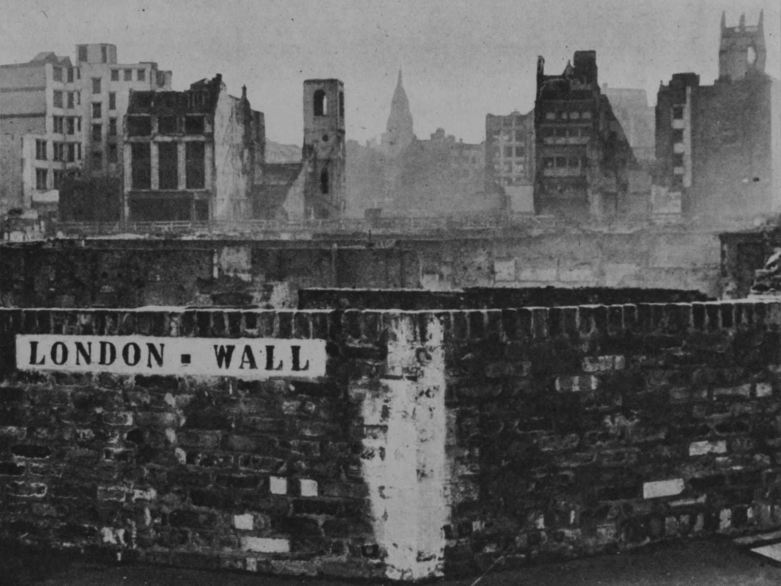 A low wall with a stencilled sign reading "London Wall" is visible with the view above it consisting of destroyed and badly damaged buildings as far as the eye can see.