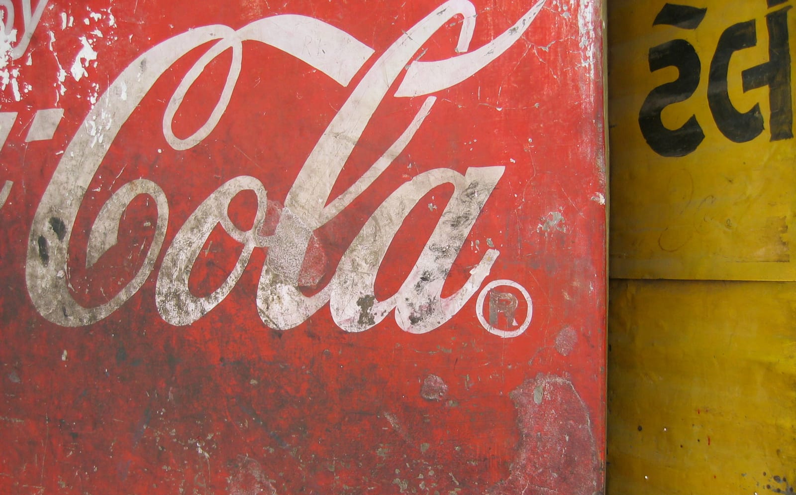 Second portion of the Coca-Cola cursive logotype in white on red, where the panel had been aged by dirt and knocks.