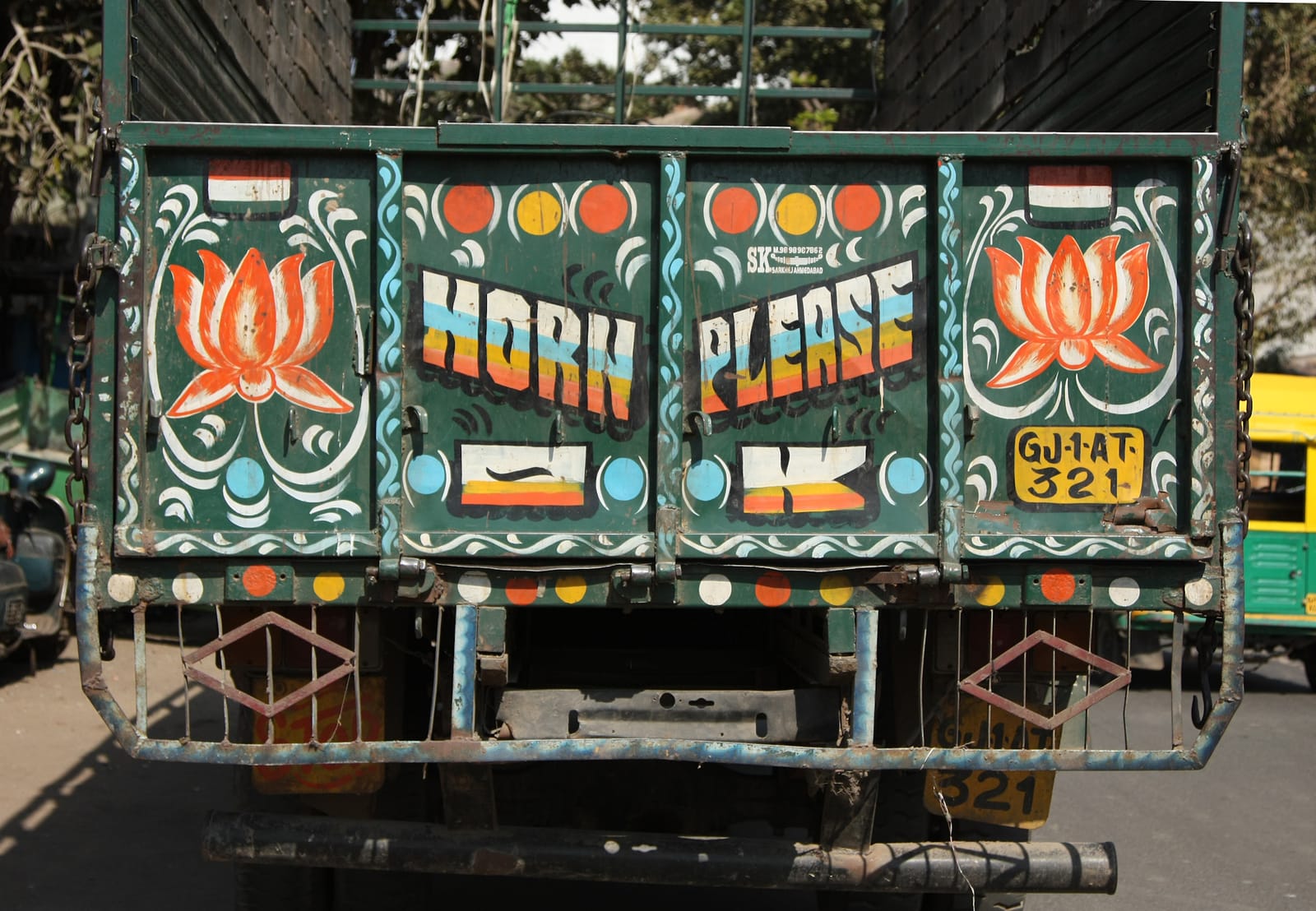 Rear and of a truck that is decorated with lotus flowers left and right, basic scrollwork, spots, and lettering in the middle that reads "horn please, OK".