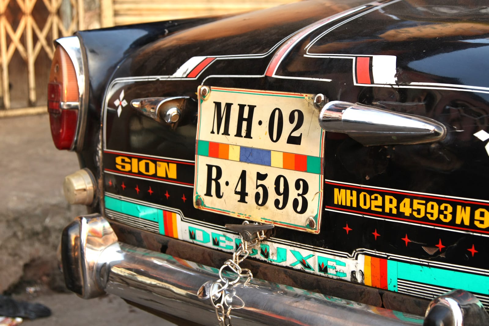 Rear end of a vintage black car with a prominent number plate and then painted decorations, including pinstriping and lettering that repeats the registration number.
