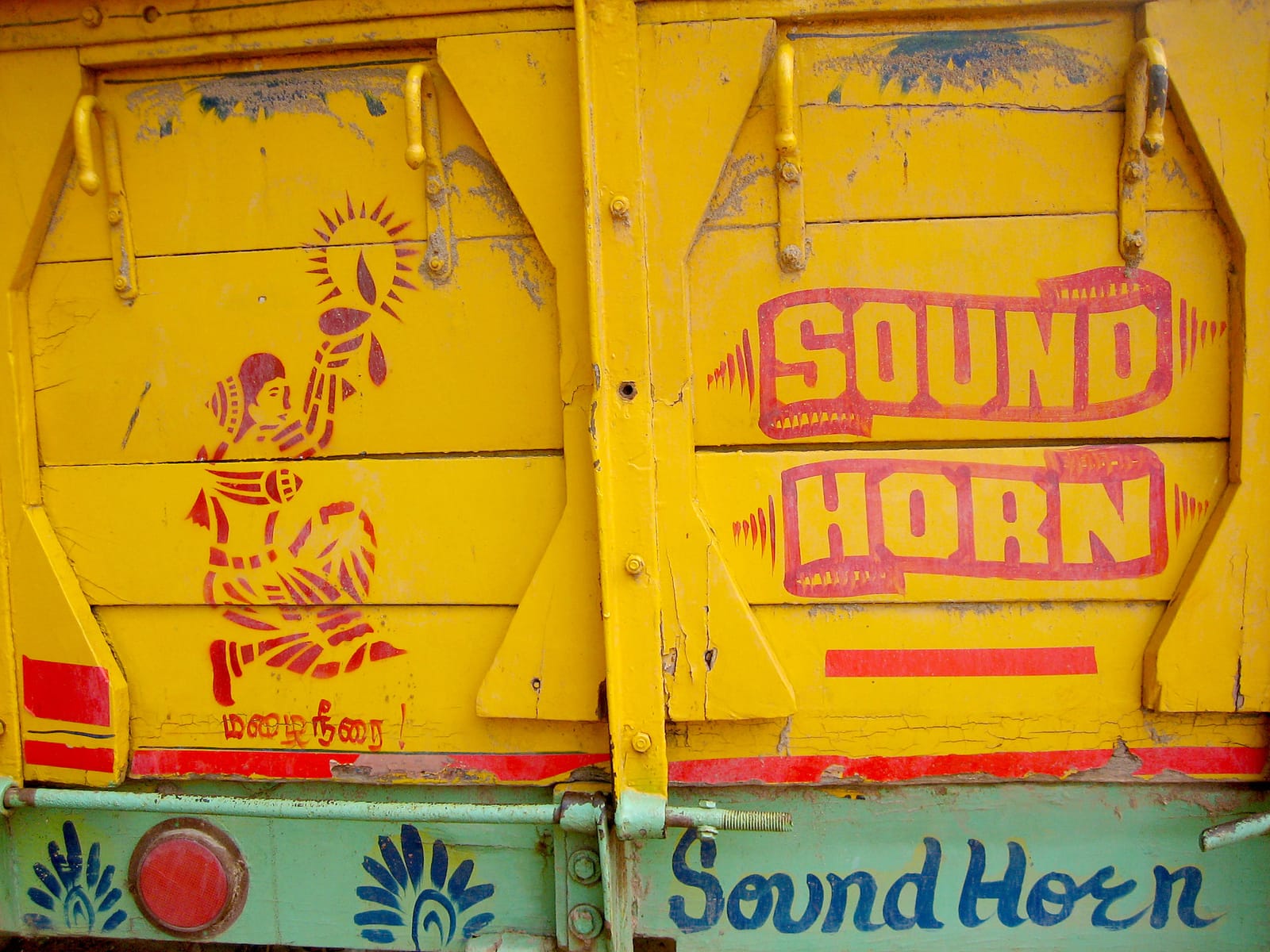 Back of a truck painted mainly in yellow with a stencil-style illustration of a woman holding a candle on the left and lettering on the right that reads "sound horn". Below is a horizontal strip in light green that repeats the "shound horn" message.