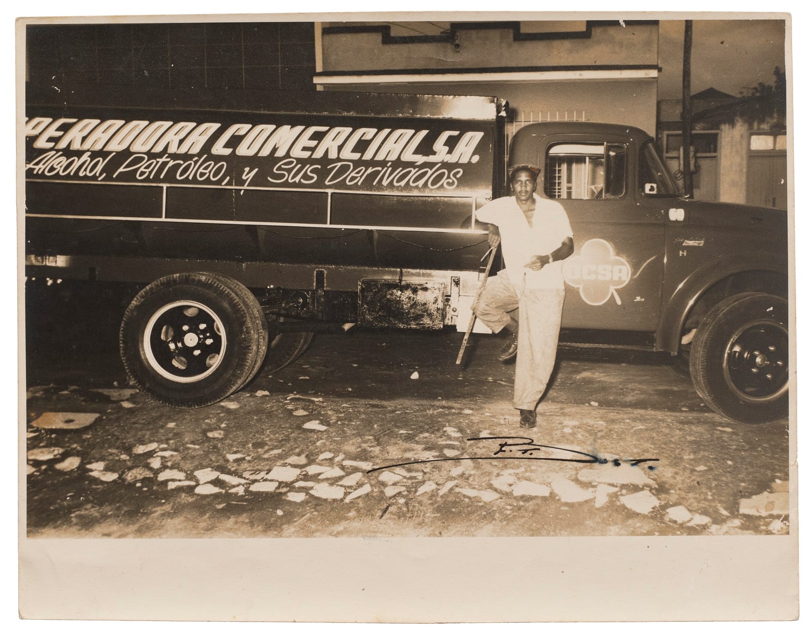 Smartly dressed man resting a foot on a lorry which is hand-lettered, and what is visible reads "...peradora Comercial S.A."