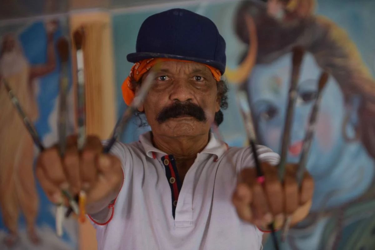 Man holding paint brushes between his fingers.