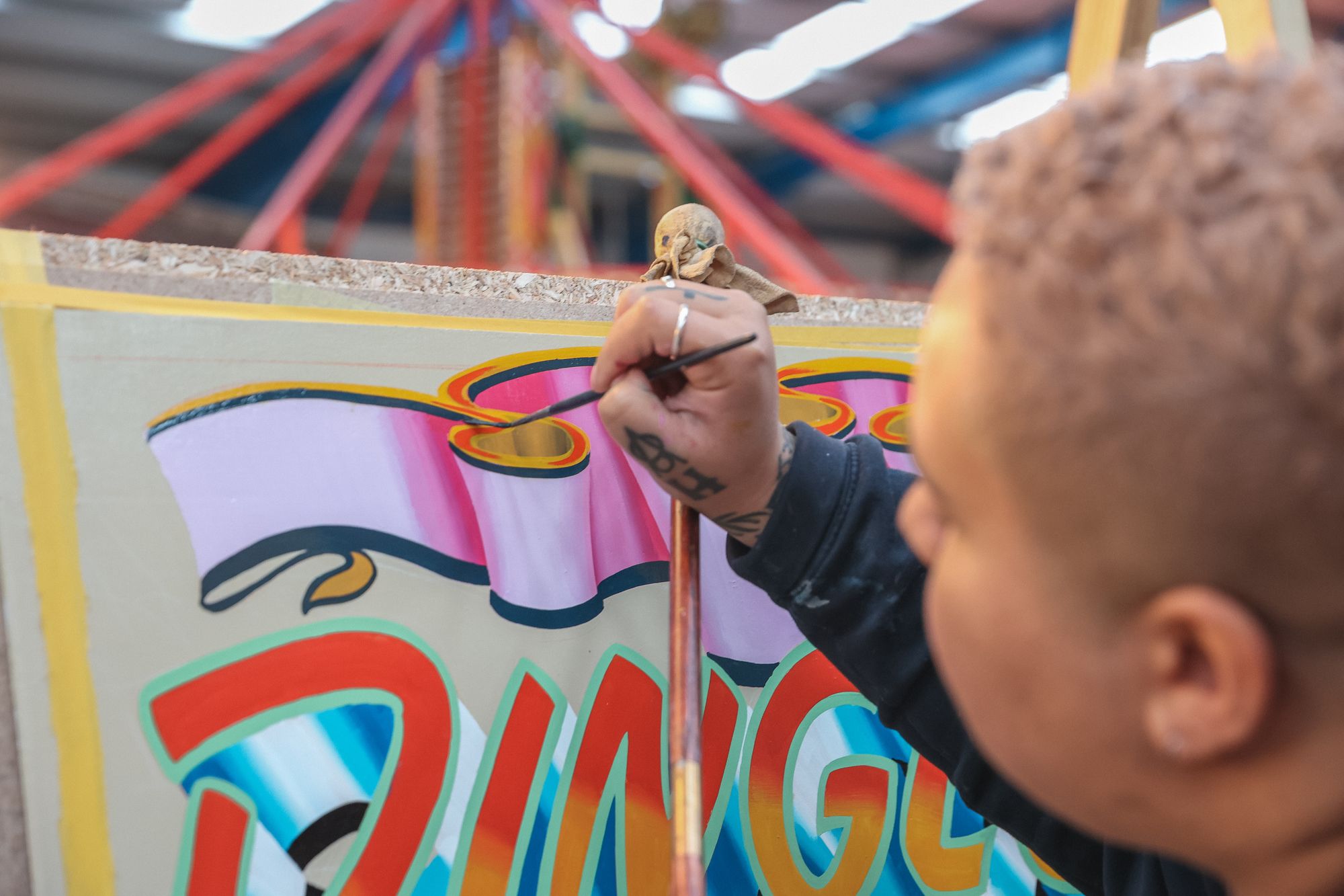 Sign painter working on scroll with brush hand resting on a mahl stick.