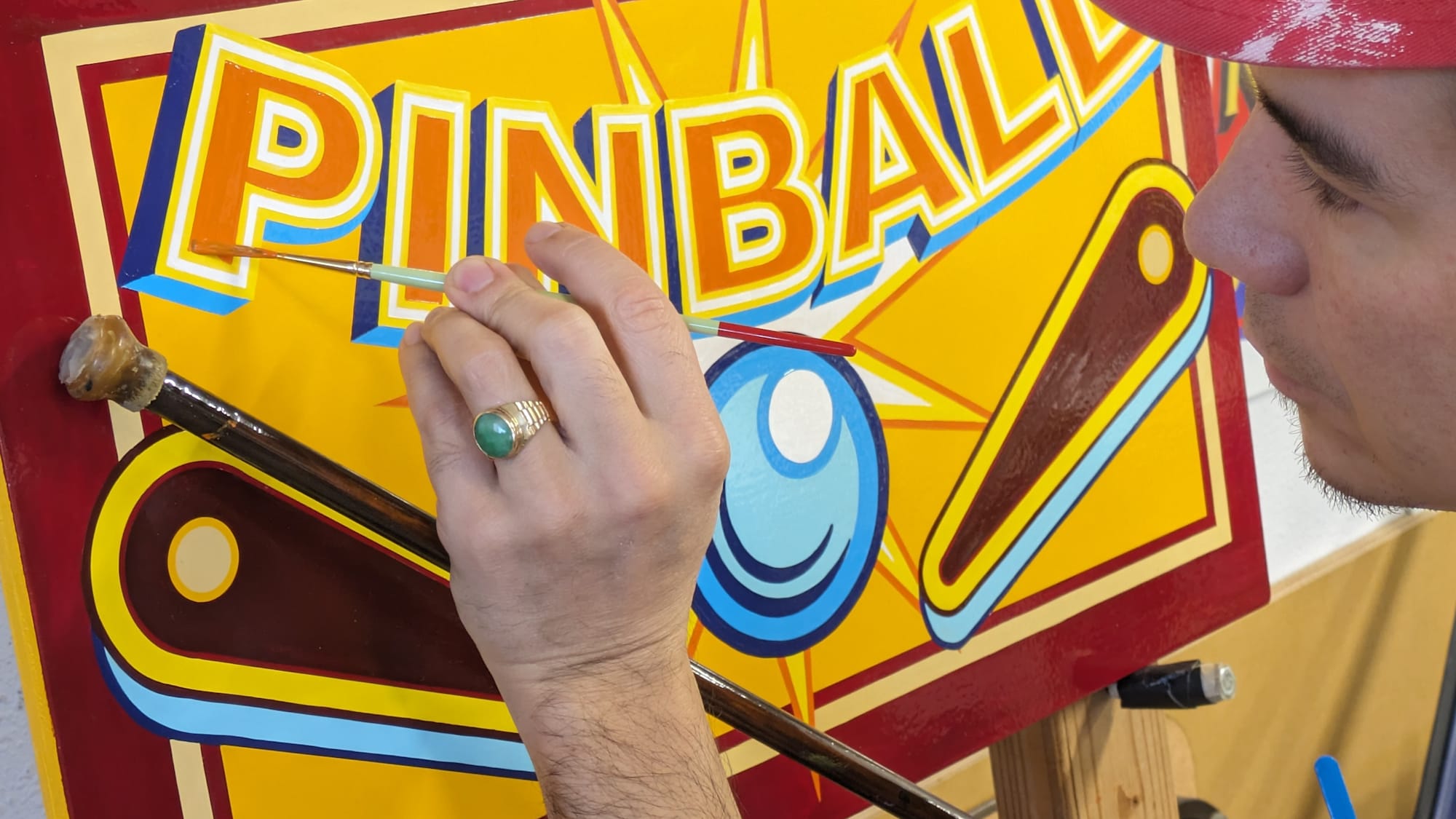 Man painting a brightly coloured sign that says 'Pinball' and has an illustration of the ball and flippers.