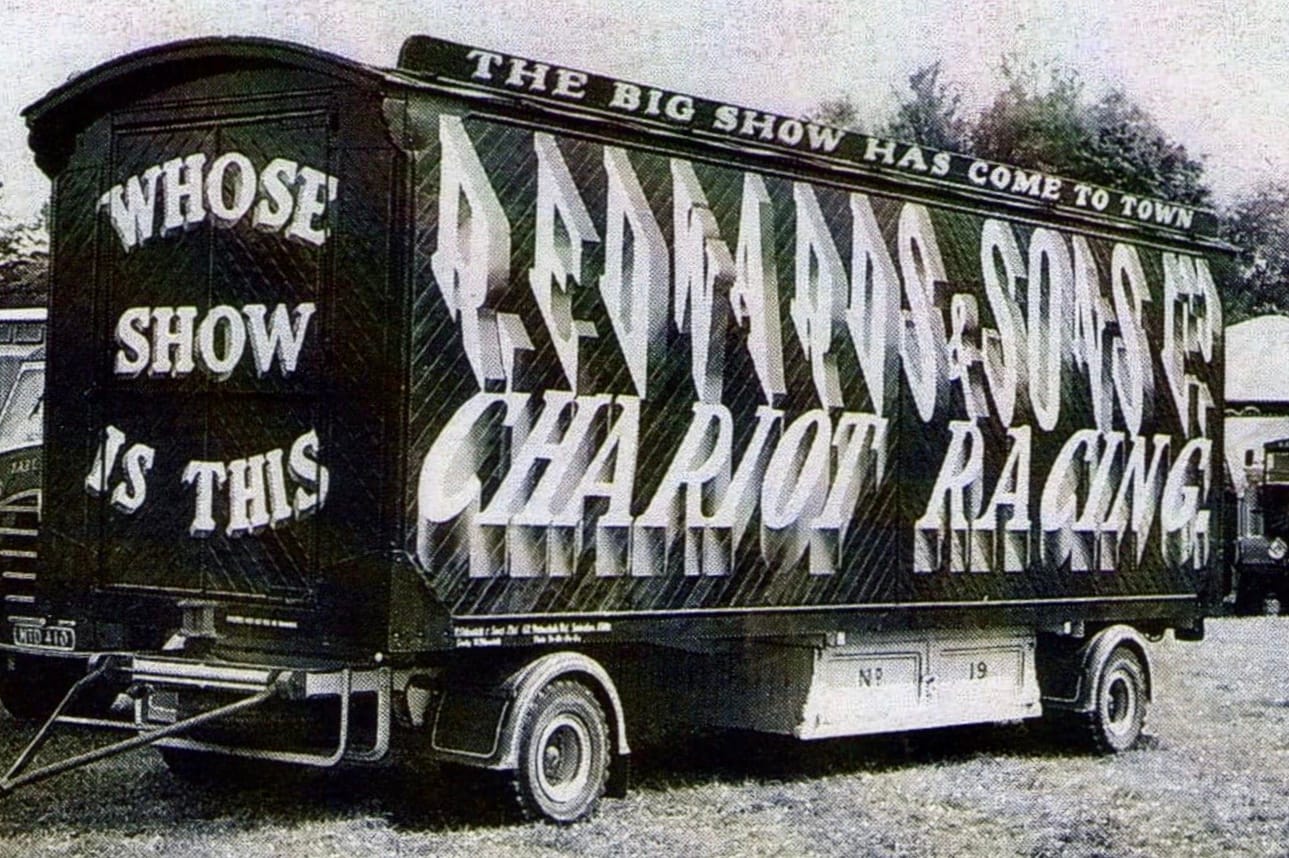 Black and white photo of a trailer decorated with flamboyant lettering advertising a fairground ride.