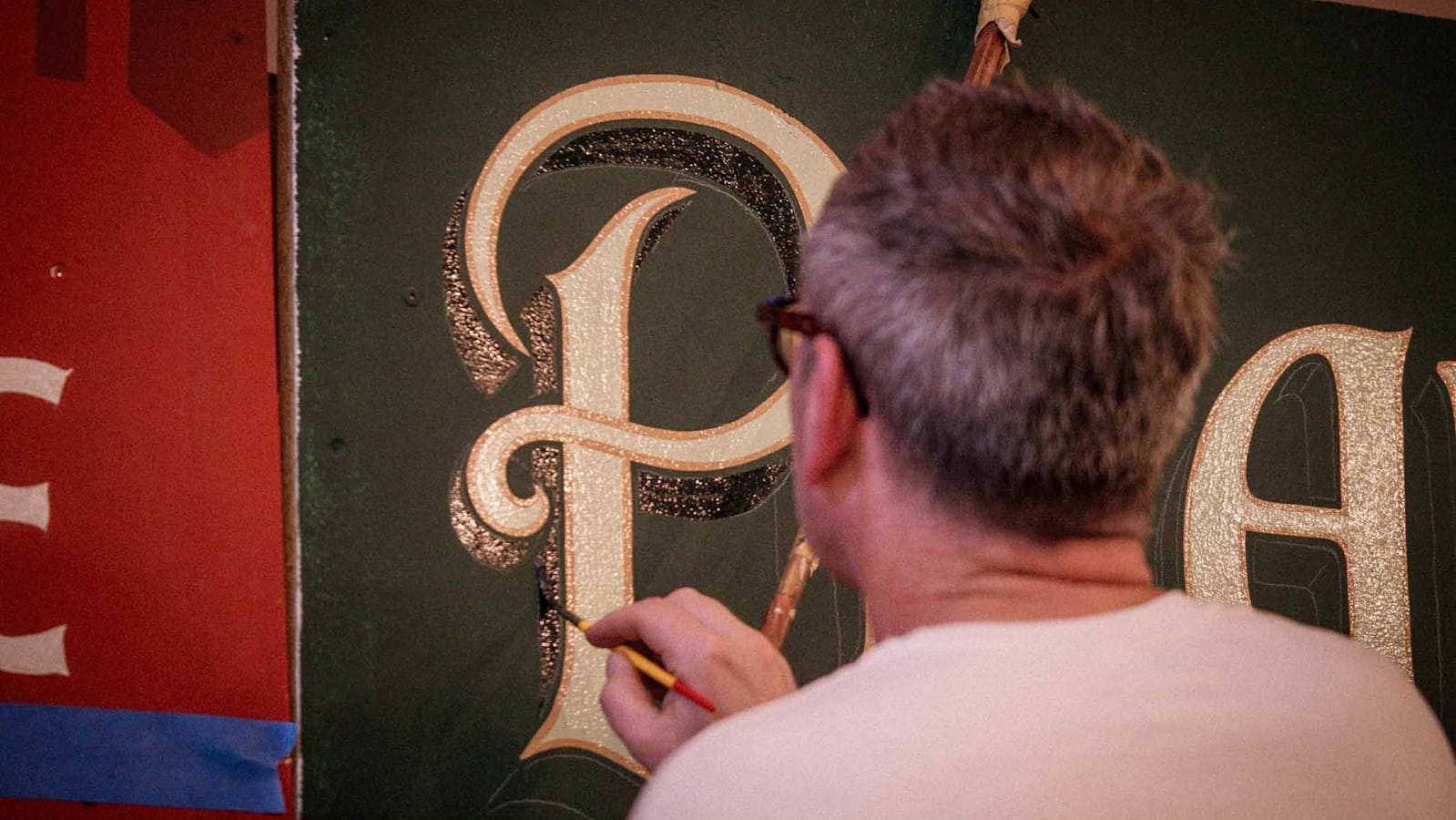 View from behind a man painting a shadow onto a letter 'P' on a sign.