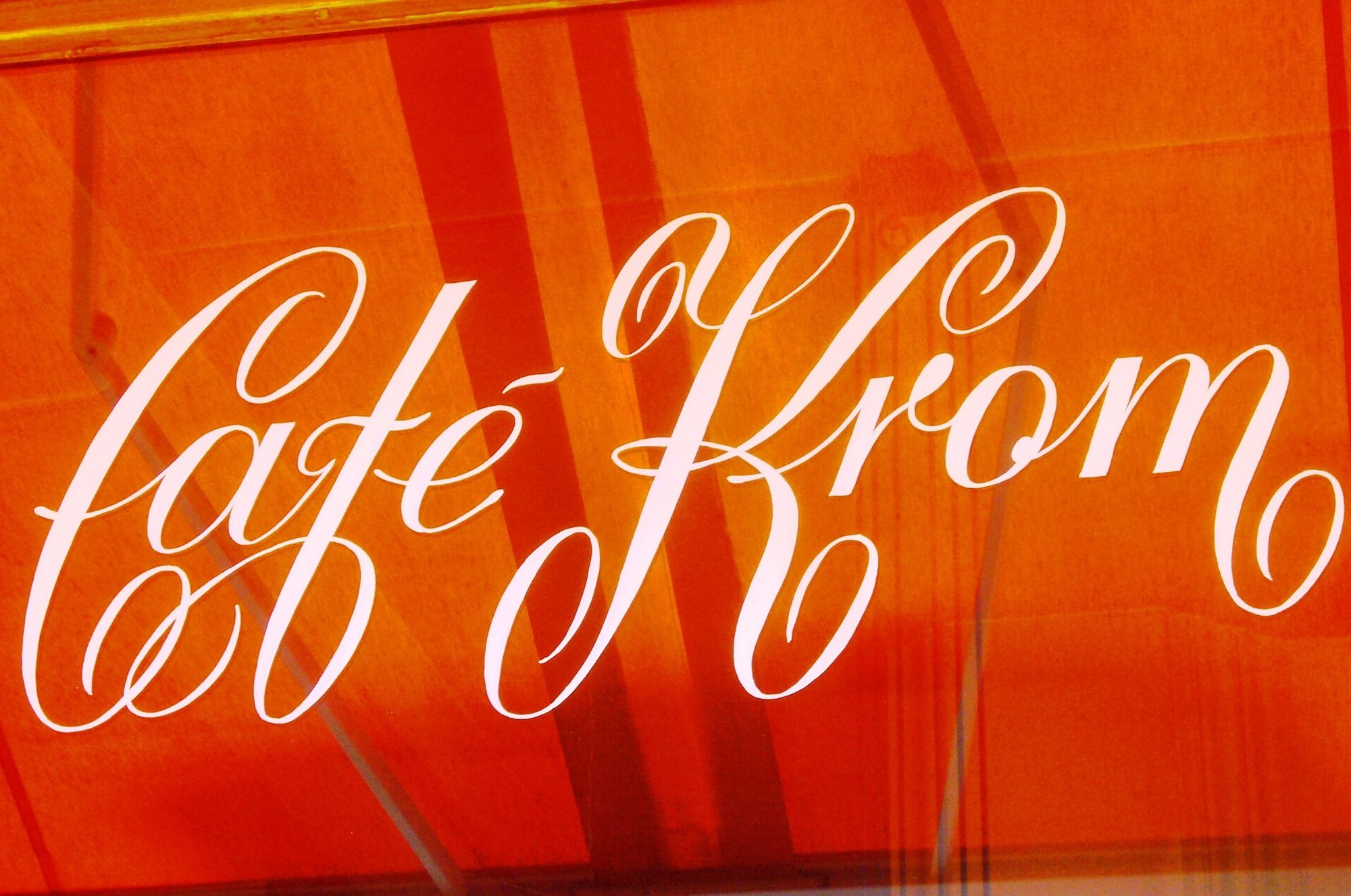 Sign painted in white by hand on a glass window reflecting an orange awning.