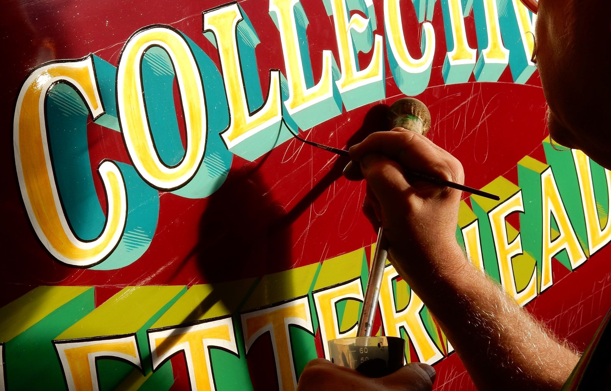 Man painting a sign that reads 'Collective Letterheads'.