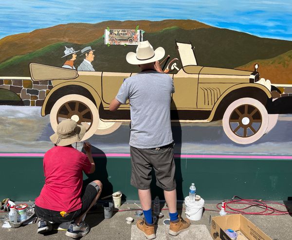 Two people painting a car on a wall.