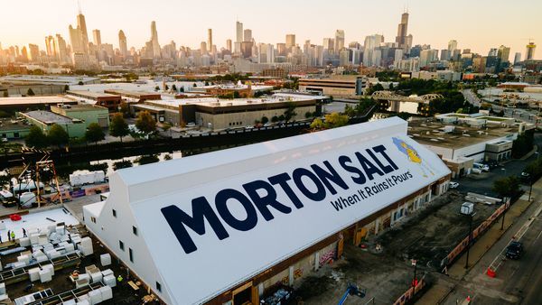 Drone photo of a large sign painted on a sloping roof with the city of Chicago in the background.