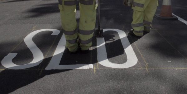 Workers painting a 'SLOW' sign in white on a tarmac road.