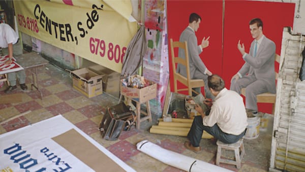 Sign shop/artist studio with man at work, and signs and paintings on the walls and floor.