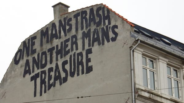 Top of a gable end wall with large black letters painted on it that say "One man's trash, another man's treasure".