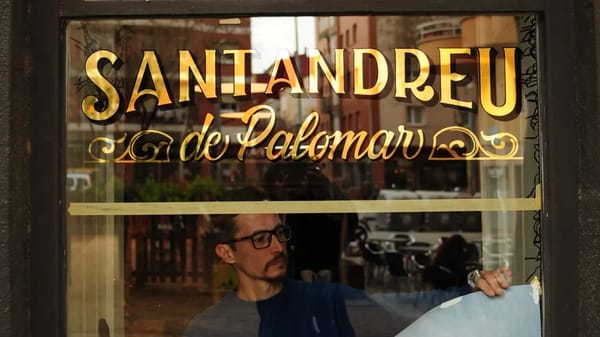 Window with gilded and shadowed sign in the upper portion, below which the sign painter is removing the pattern.