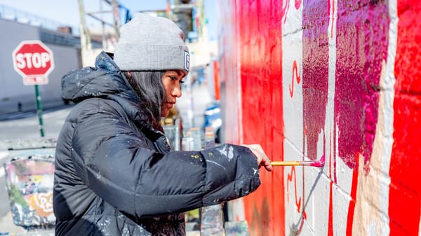 Woman painting the colour purple on a portion of a wall with other portions already painted in red and white.