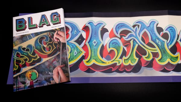Magazine cover with a person painting flamboyant lettering under the masthead. It’s set on a poster of the same lettering.