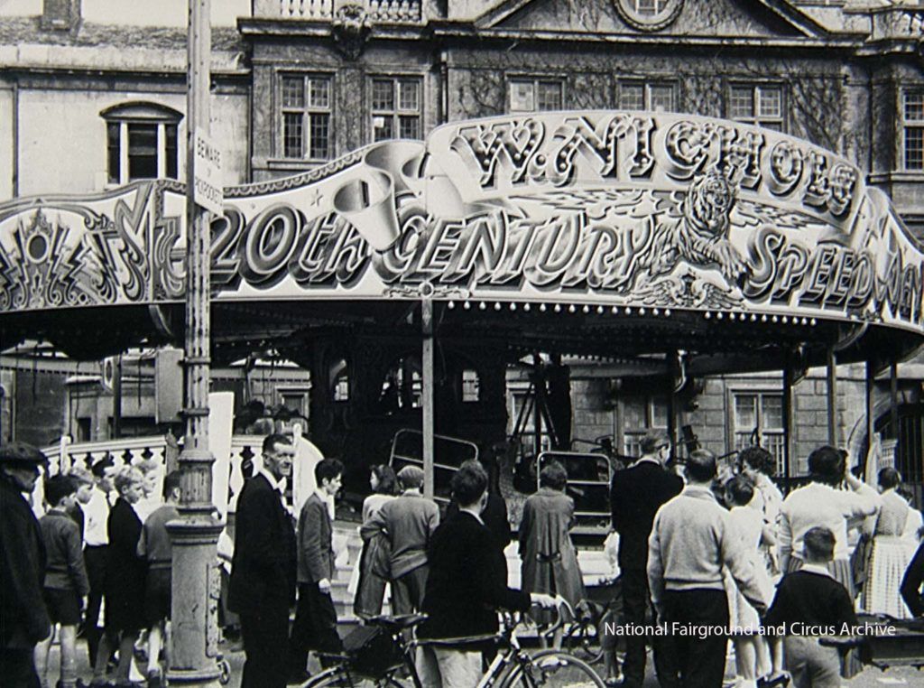 Archival black and white photo of people at a fairground in front of the 20th Century Speedway ride.