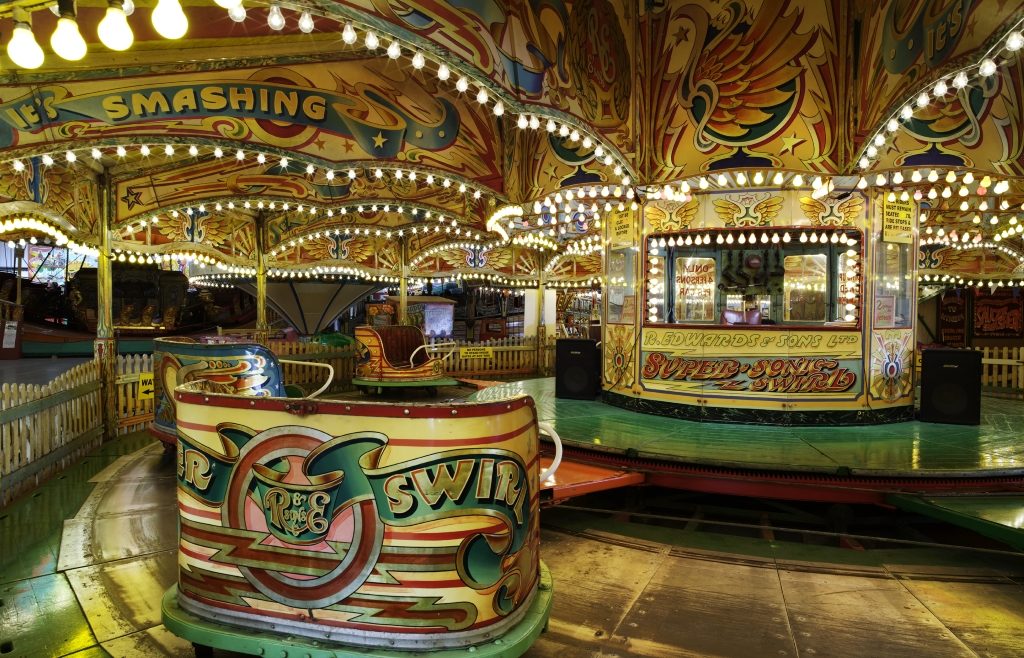 Fairground ride with hand-painted decorations and lettering illuminated at night by lightbulbs in the top of the ride.