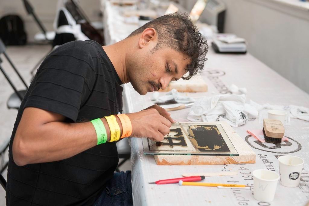 The W&B Gold Leaf Gilding Zone allowed letterheads to try their hand at reverse-glass gilding under the guidance of Chris Surdivant (Debonair Sign Man) and Ash Bishop (Brilliant Sign Company), along with guest appearance from many others including Noel Weber and Eddy Artist. Here’s Hanif Kureshi working on the back of his glass piece.