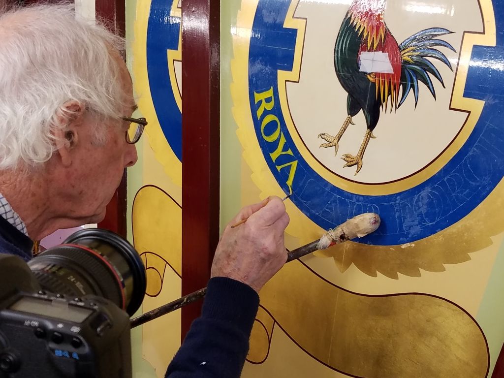 Main painting lettering onto a sign with a pictorial of a cockerel.