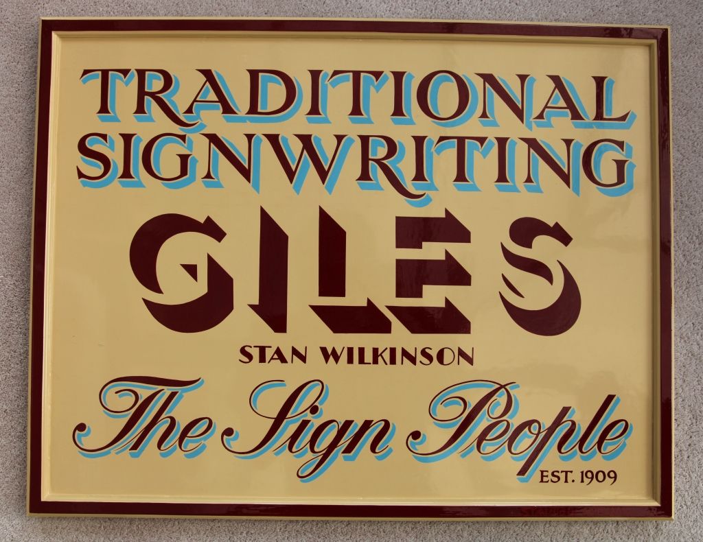 Hand-painted lettering on a sign board advertising the traditional signwriting services of Giles the Sign People.