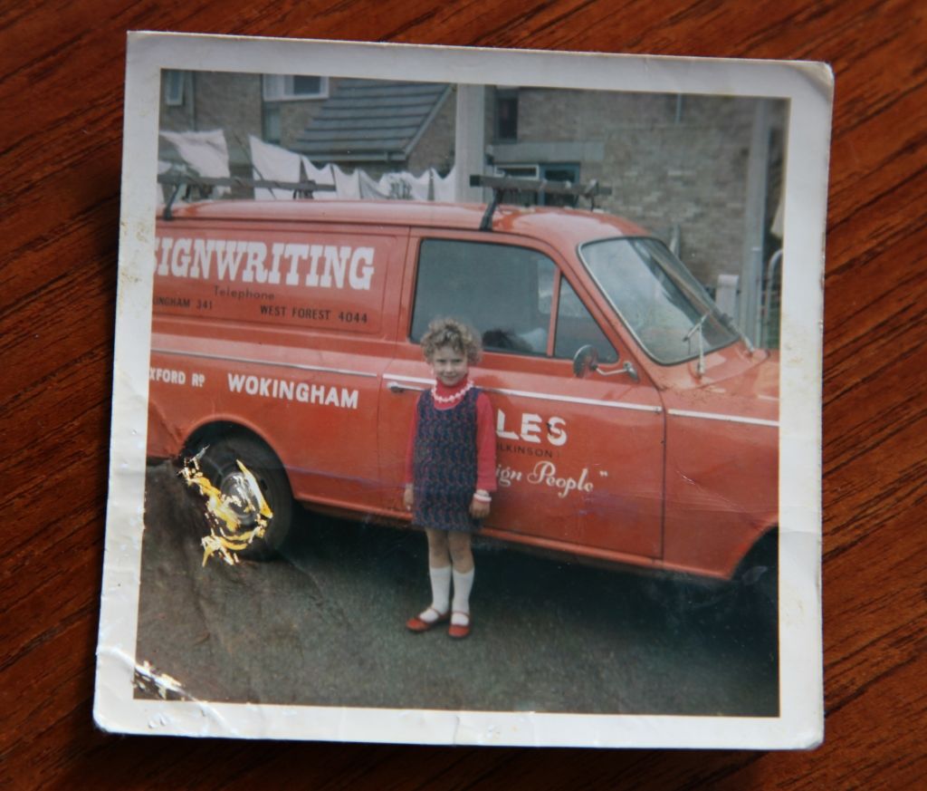 Girl standing in front of a red van with the hand-painted word 'signwriting' on the side.
