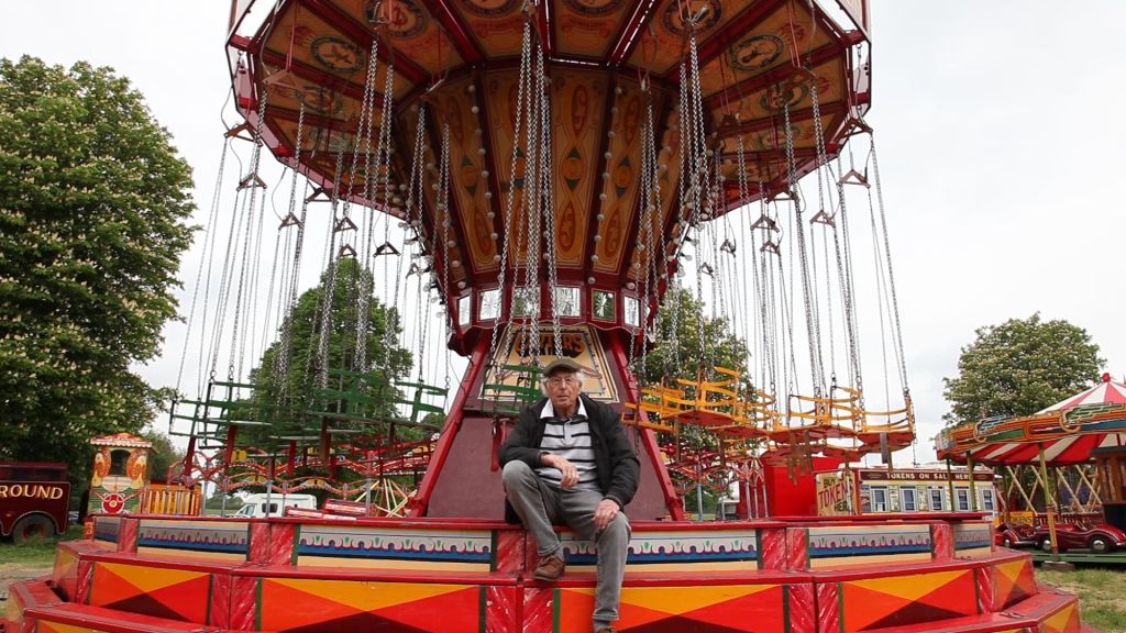 Man sat on the edge of a fairground ride with trees in the background.