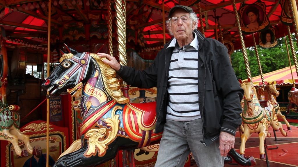 Man posing in front of a painted horse from a fairground ride.