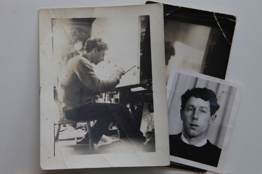 Archival photos on a table, with one showing a young man painting a sign at an easel.